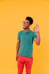 Excited man with funny hairstyle posing with okay sign. Indoor shot of emotional african guy in glasses and green t-shirt.