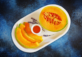 Sweet melon cut into slices with honey and lavender on a white plate