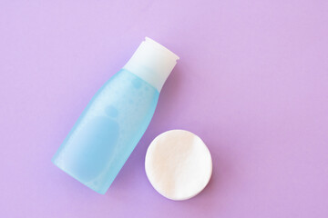 Top view of facial toner and round cotton pads on purple background with copy space. Blue liquid tonic or make up remover for face care