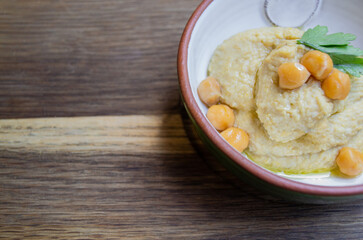 Hummus decorated with parsley and chickpea peas in a ceramic bowl on a wooden background. Copy space
