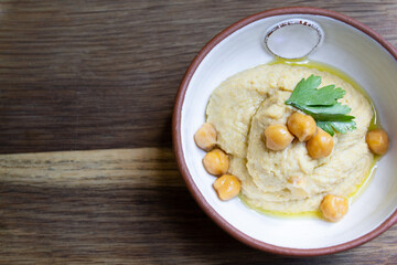 Hummus decorated with parsley and chickpea peas in a ceramic bowl on a wooden background. Copy space
