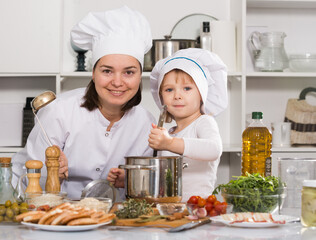 Happy girl and her mother are standing with ladle and soup together in the kitchen at home.