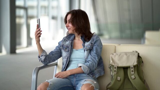 woman in airport, taking photo by smartphone in terminal, sitting in departure area