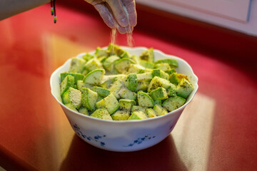 Raw courgettes diced in a bowl and a hand that spreads breadcrumbs.