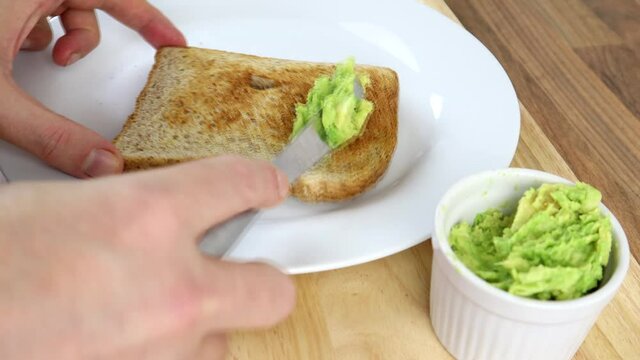 Mashed Avocado Being Spread On Brown Toast