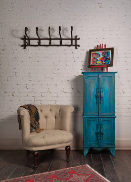 Classic beige armchair with wooden legs, vintage turquoise cupboard, wall hanger, and ornate scarf on white bricks wall and grunge wooden parquet with red decorated carpet