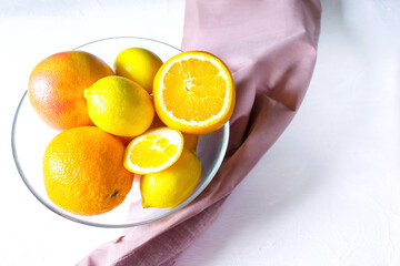 Citrus fresh fruits on plate, bow with napkin, juicy lemon, oranges on white table with copy space