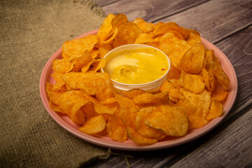 Potato chips on a round platter and a saucepan with cheese sauce. Close up.