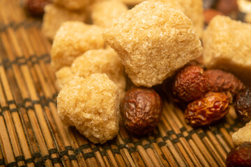 Pieces of brown cane sugar and dried rosehip fruit scattered on a reed Mat. Close up.