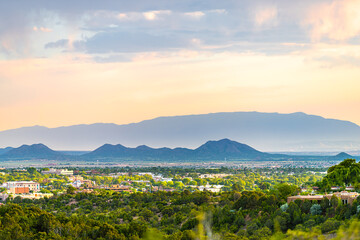 Naklejka premium Zachód słońca w Santa Fe, Nowy Meksyk, panoramę miasta ze złotym godzinnym światłem na letnich roślinach zielonych liści i budynkach miejskich z sylwetką gór