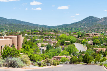 Fototapeta premium Widok na panoramę miasta w Santa Fe w Nowym Meksyku w górach drogi przez sąsiedztwo społeczności z zielonymi roślinami latem i tradycyjnymi domami adobe