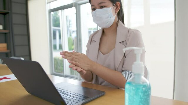 Asian women wear face mask and cleaning hand sanitizing by alcohol gel before start work with laptop computer. New normal, social distancing measure and working lifestyle after corona virus crisis.
