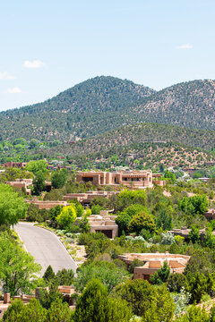 Vertical landscape view in Santa Fe, New Mexico mountains of road street through community neighborhood with green plants summer and adobe traditional houses