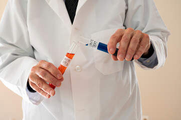 Reseracher in a labcoat about to pour liquid from one Covid  test tube to another.