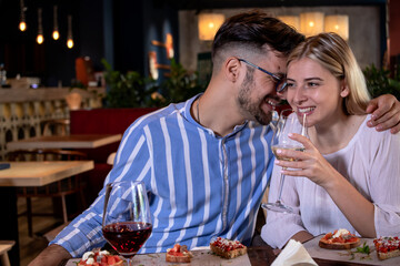 Happy young romantic couple laughing and toasting with wine glasses at dinner in a beautiful fancy...