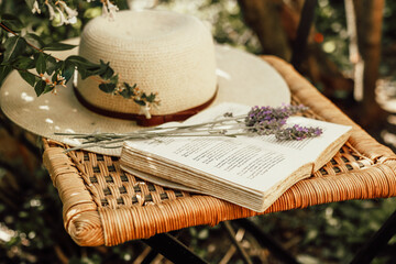 Lavender bouquet on open book and womens summer hat on old wicker chair in garden, nature and slow...