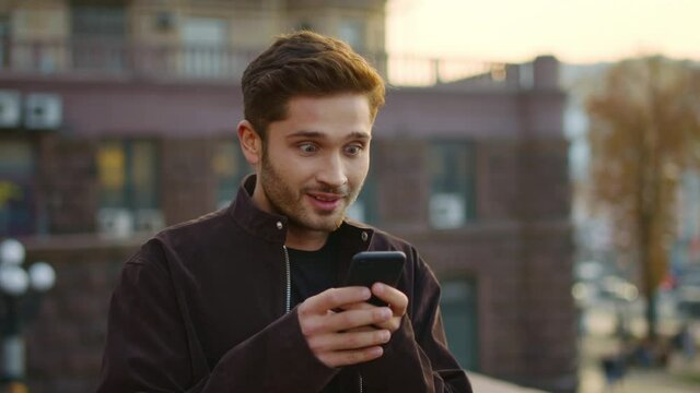 Euphoric guy receiving message phone outdoors. Excited man gesturing like winner
