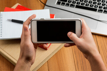 Student using a smart phone. Laptop, books and office supplies