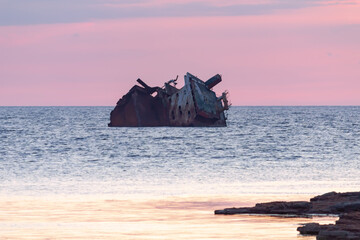 sunken rusty old ship at sunset, in the foreground rocks