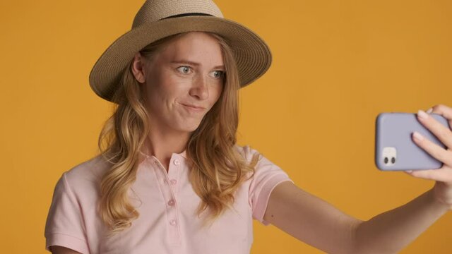 Attractive stylish blond girl in hat waving no gesture recording video on smartphone over colorful background
