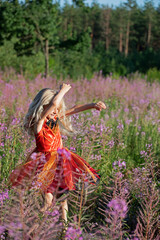 cute little blonde girl in an elegant fairy dress whirl in the flowers of fireweed forest. Evening sun rays. Festive mood, birthday during the global pandemic, Coronovirus.