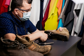 Fototapeta premium Cobbler with face mask repairing old pair of shoes. Covid-19 concept. Shoemaker doing his job in shop.