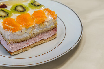 home-cooked biscuit cake with a layers of home-made cottage cheese decorated with tropical fruits on white plate