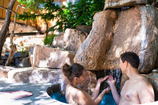 Young woman man romantic couple relaxing swimming in cold plunge stone rock waterfall in Japanese spa pool with colorful blue water in Japan onsen