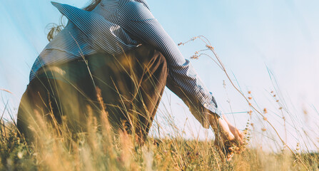 Section of a person squatting in a field, watching the sunset, wind blowing the shirt