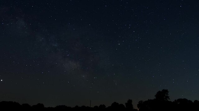 Time lapse of the Milky Way crossing the night sky over a silhouetted rural landscape