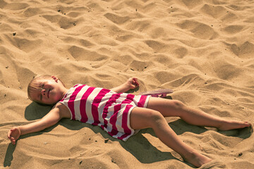 Baby girl lying on sand. Adorable kid sunbathing at summertime. Young child resting and relaxing...