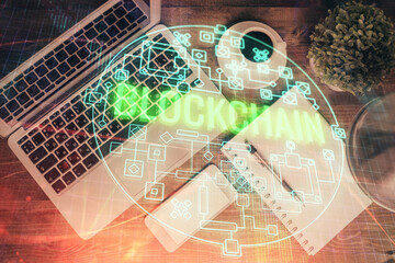 Blockchain theme hologram drawings over computer on the desktop background. Top view. Double...