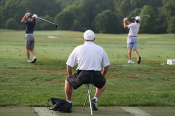 A man watches tournament golfers warm up on the driving range.