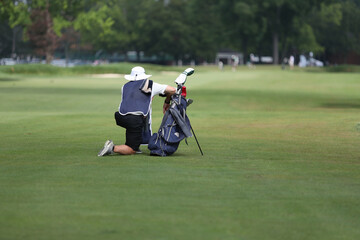 A golf caddie kneels down in the fairway