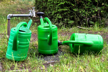 Fototapeta na wymiar Three green watering cans stand and lie beside the tap in the grass