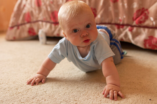 a newborn boy wearing blue clothes lies on the floor in the parent's bedroom and looks at the camera
