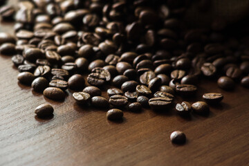 Coffee spills out of the bag onto the table. Arabica and robusta on a dark wood table. Brown color. Coffee beans scattered on the surface. Place for the text.
