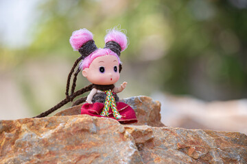 The doll's full frame with nature has a blurred background.
