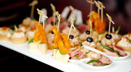 catering made canapes of cheese and orange and pieces of meat on spoons