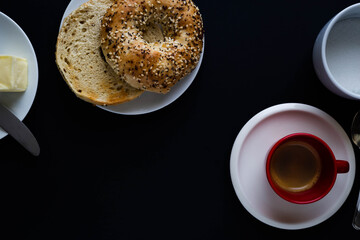 Toasted multigrain bagel with butter and table knife on black background with espresso coffee and sugar.