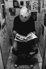 Bizarre portrait of a guy with lemon mask reading the newspaper in an old and scratched bathroom...