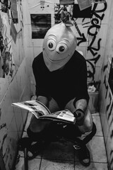 Bizarre portrait of a guy with lemon mask reading the newspaper in an old and scratched bathroom...