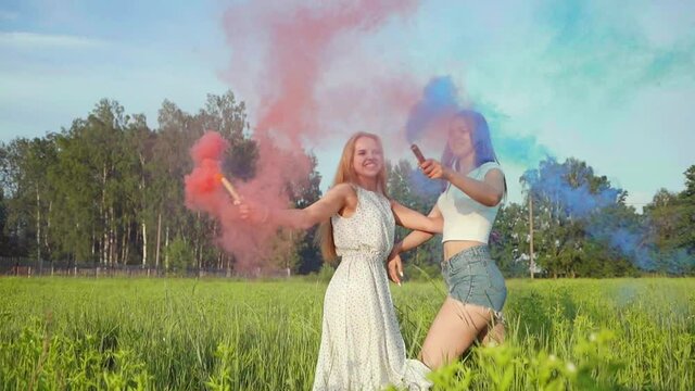 Two happy girls spray colorful smoke.