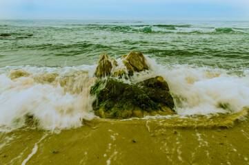 Waves rushing to shore over a large boulder
