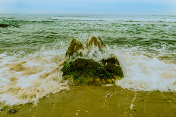 Waves rushing to shore over a large boulder