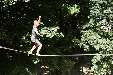 Young caucasian slackliner man doing slackline in the forest on a summer day.