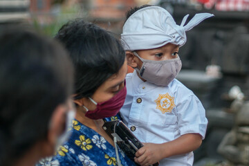 Fototapeta na wymiar Balinese mother and child are wearing traditional clothes during the corona pandemic or covid-19. They both use masks to protect themselves from virus attacks. They prepare to pray at the temple
