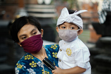 Balinese mother and child are wearing traditional clothes during the corona pandemic or covid-19. They both use masks to protect themselves from virus attacks. They prepare to pray at the temple