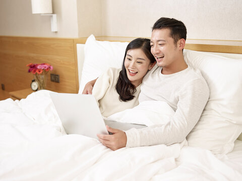 young asian couple staying at home watching movie in bed