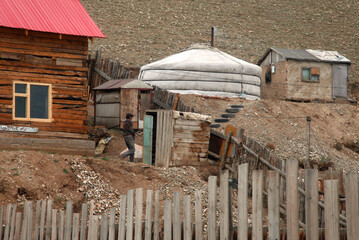 A portable yurt sits next to an outhouse and wooden home on a hillside in UlaanBaatar, Mongolia.
